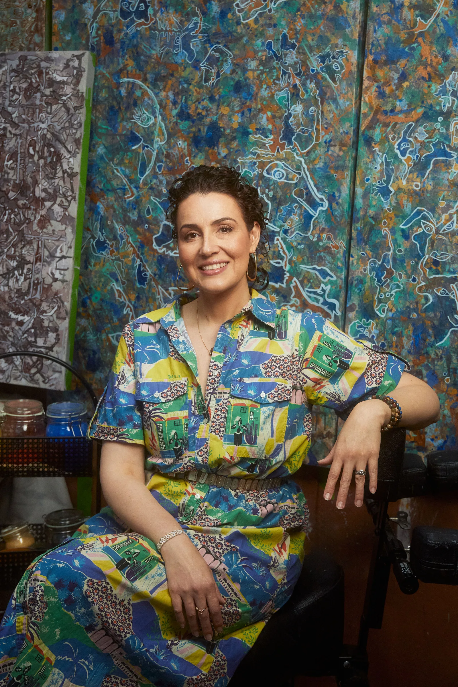 Ana Violeta Horta seated in her studio in a patterned dress, surrounded by her natural pigment paintings